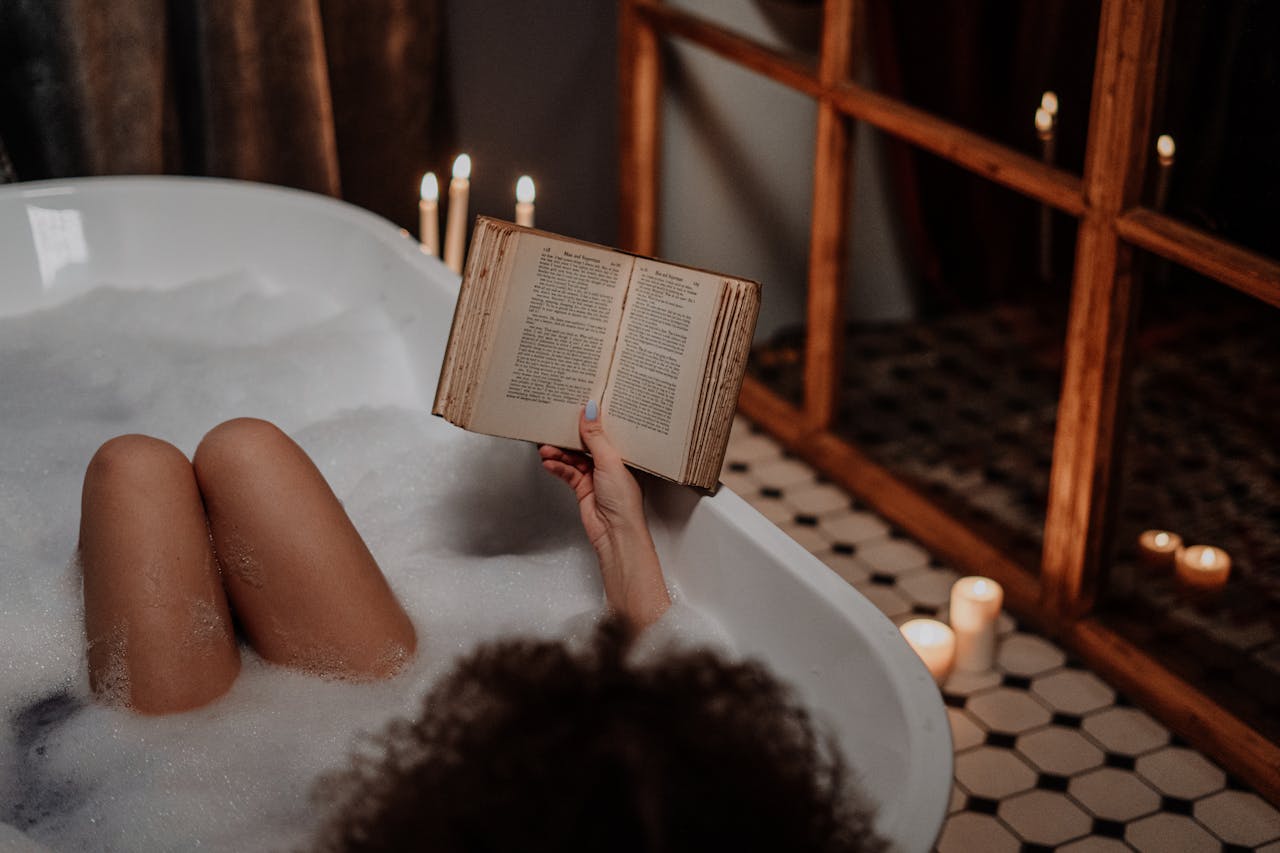 A peaceful scene of someone enjoying a bubble bath while reading by candlelight.